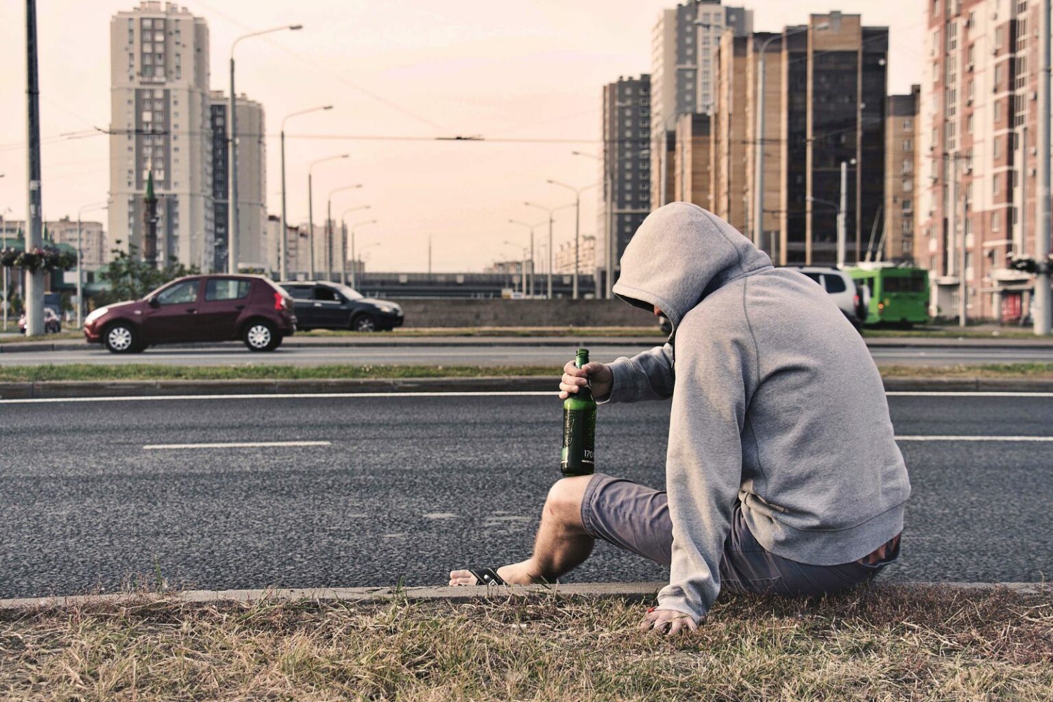 알콜 의존증, 남성이 술병을 들고 차도 옆에 앉아있는 이미지